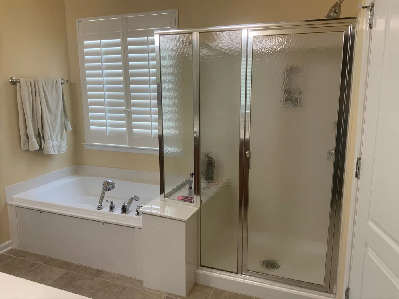 Alcove tub beside a framed glass shower door before remodeling