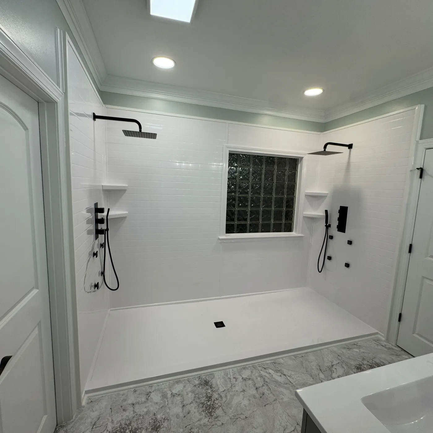 Large white walk-in shower with two shower heads and a glass block window after remodeling