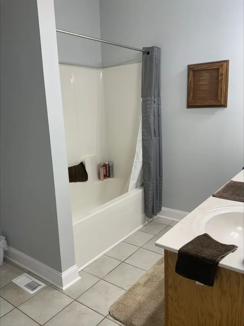 White tub and shower combination with a curtain rod before remodeling