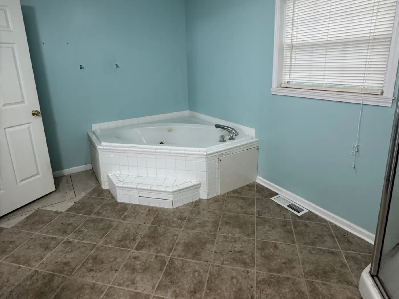 Dated corner jetted tub in a blue bathroom before remodeling