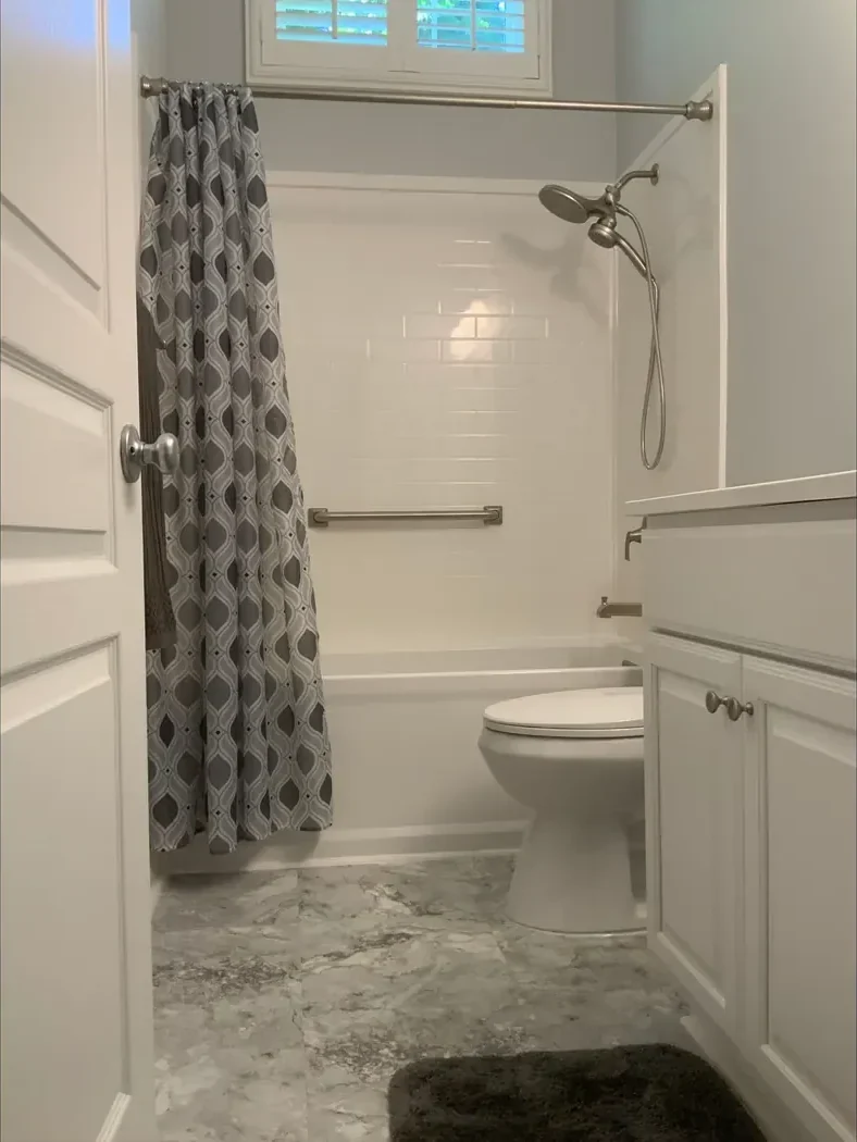 Rebuilt tub and shower with new white surfaces and a grab bar after remodeling