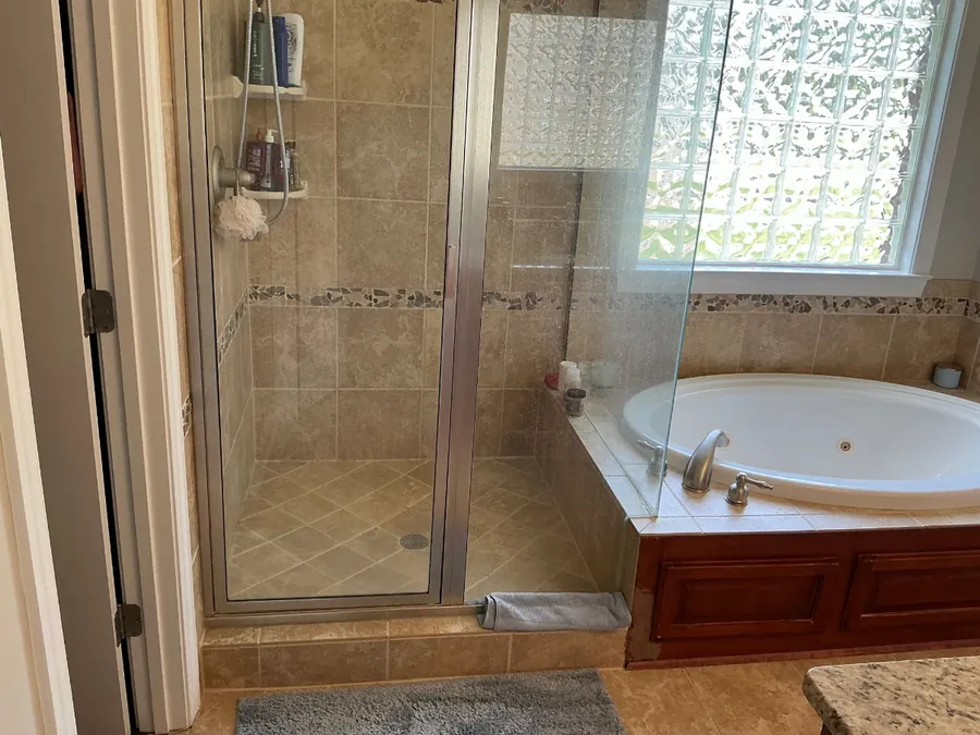 Tan tile shower with a metal door next to a jetted tub before remodeling
