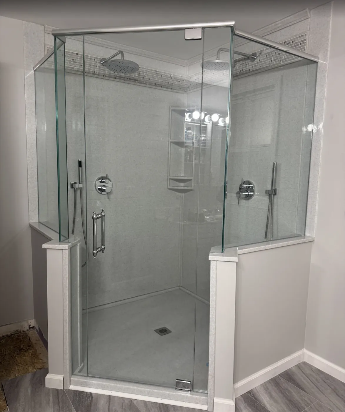 Large corner shower with clear glass panels and two shower heads after remodeling